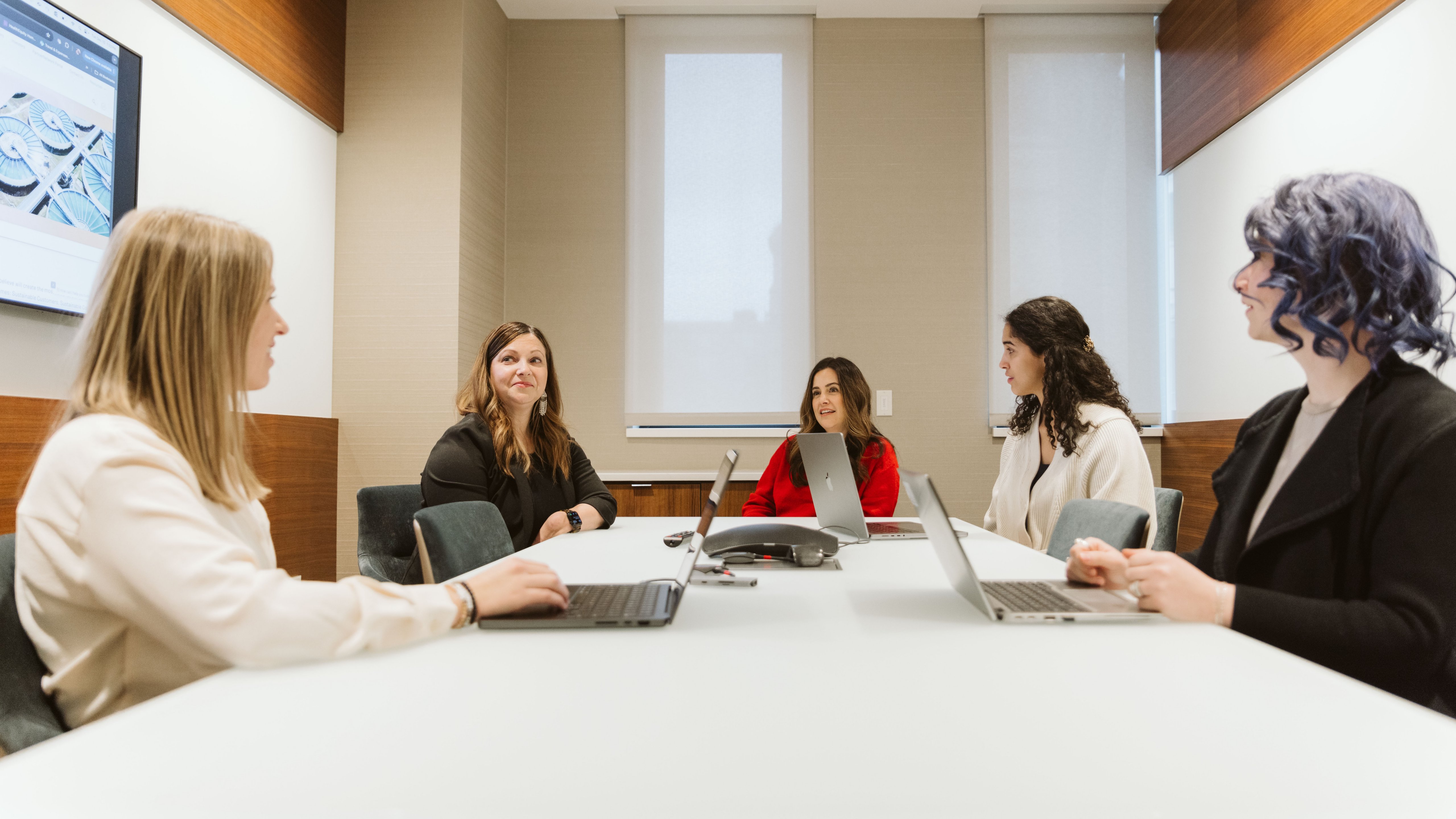 Five colleagues in a conference room with laptops, engaged in a meeting
