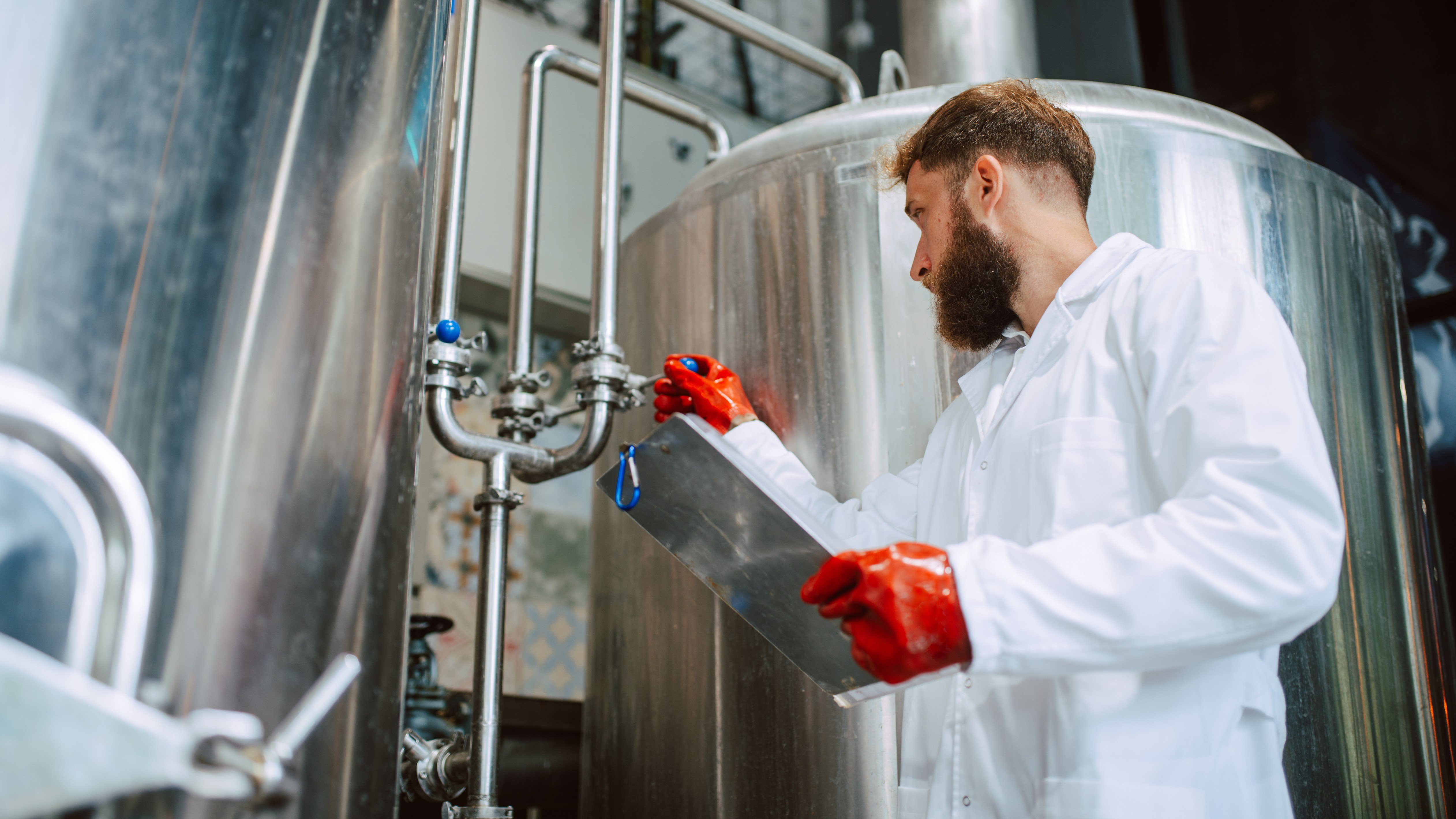 Caucasian male professional technologist expert in white suit operating production machine in food factory and doing quality control and holding checklist. Checking production in food industry