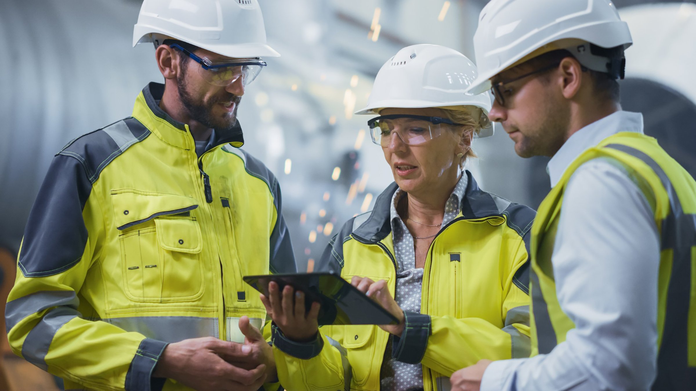 Three Heavy Industry Engineers Stand in Pipe Manufacturing Factory, Use Digital Tablet Computer, Having Discussion. Large Pipe Assembled. Design and Construction of Oil, Gas and Fuels Transport Pipeline