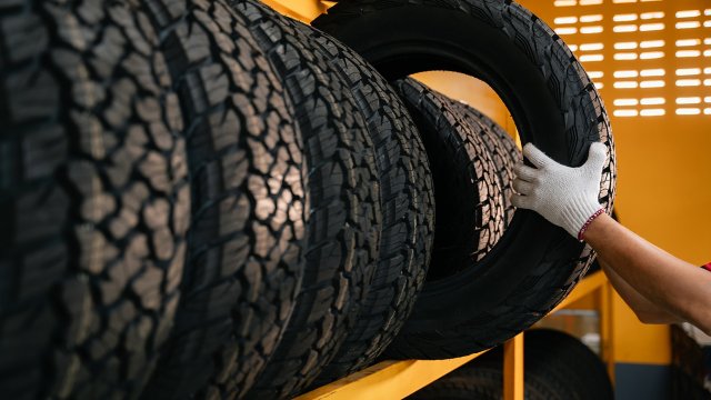 Die Hand eines Reifenmonteurs hebt einen Autoreifen aus einem Lager.
