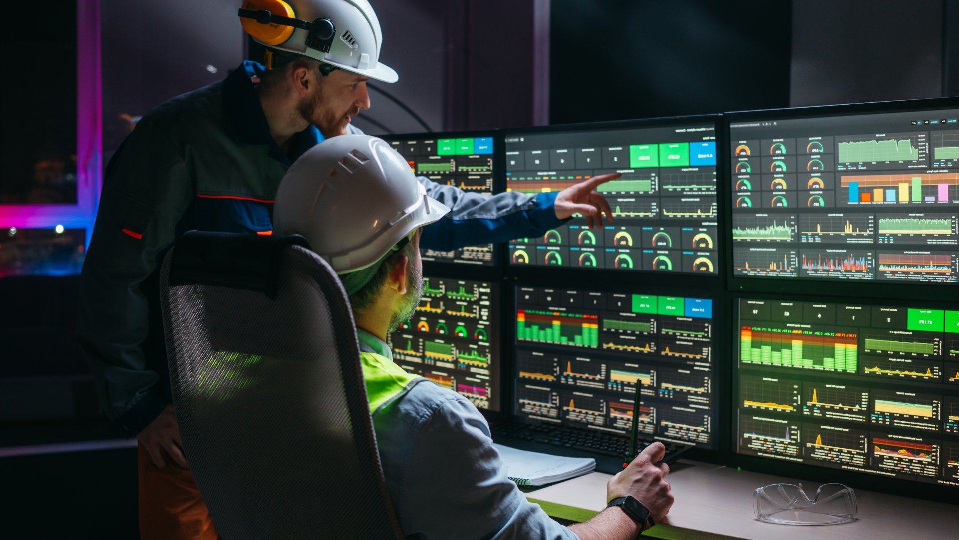 Head engineer and factory operator wearing safety vests and hard hats wollowing product process on factory uses SCADA system and industry 4.0. Two operators controll assembly line using screens with human-machine interface
