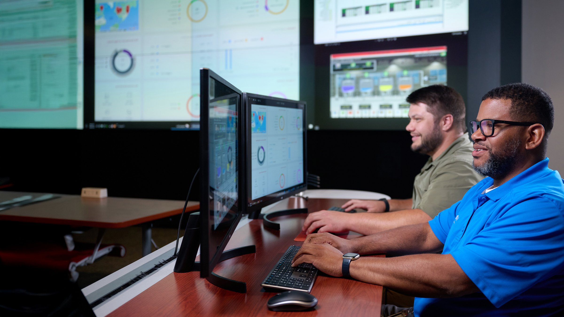 Two male engineers in a Rockwell Automation technical support center look at computer monitors as they monitor customers' critical applications and provide remote troubleshooting to minimize downtime