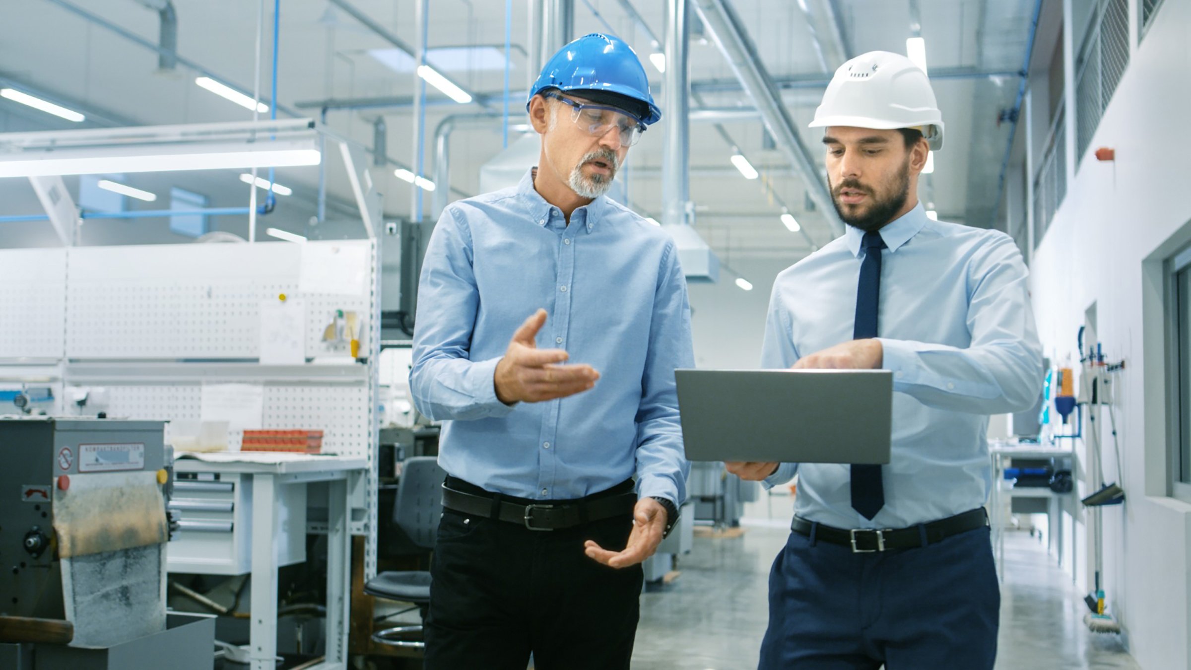 Head of the Department Holds Laptop and Discuss Product Details with Chief Engineer while They Walk Through Modern Factory.