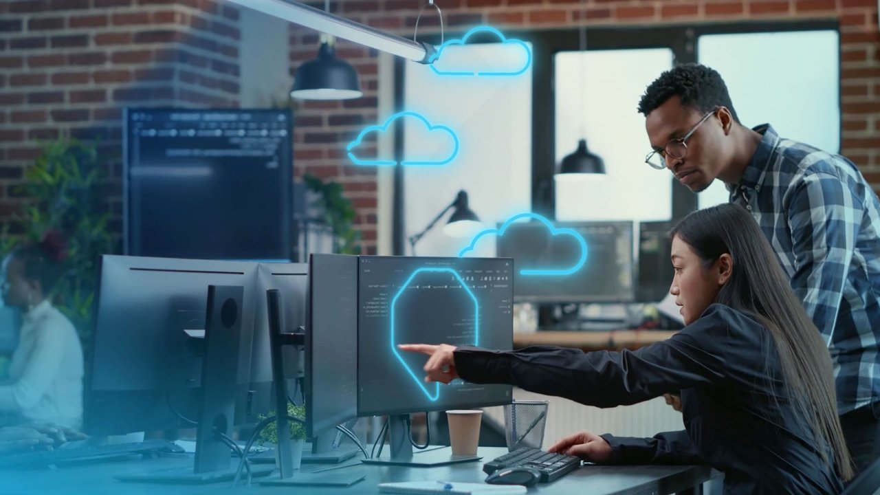 Two people looking at monitor, woman is pointed to screen, cloud icons