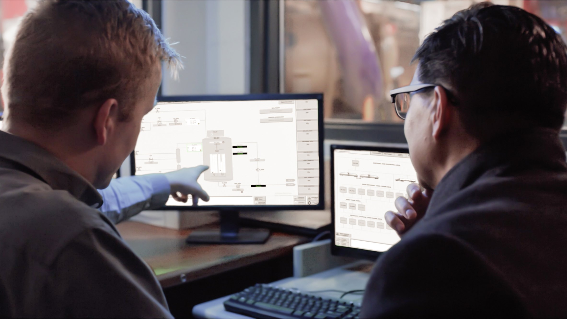 Two engineers in control room looking at monitors displaying the IntelliCENTER motor control center smart technology. Screen grabs from Intelligent Packaged Power video