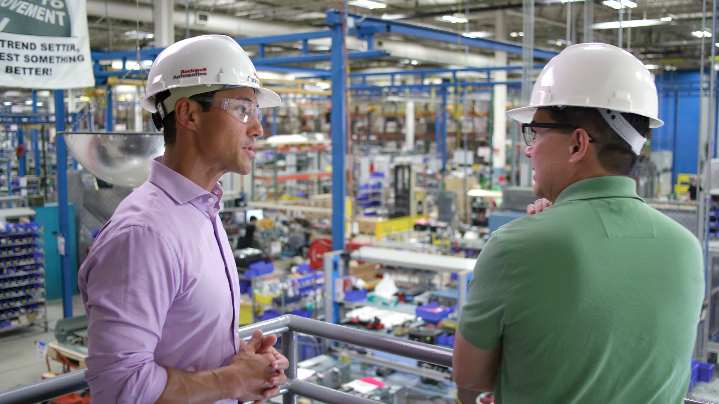 Un spécialiste de la gestion des actifs industriels de Rockwell Automation, portant un casque de chantier blanc et une chemise, conseille un client portant un polo vert sur les stratégies de maintenance, de réparation et d’optimisation des actifs, alors qu’ils surplombent l’atelier. 