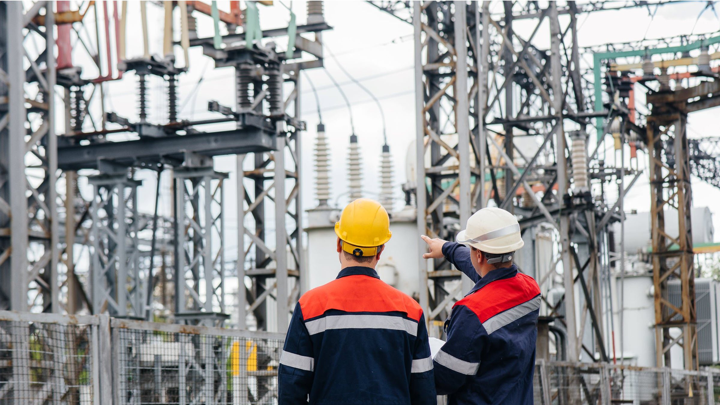 two-workers-in-hardhats-standing-before-power-transmission-towers