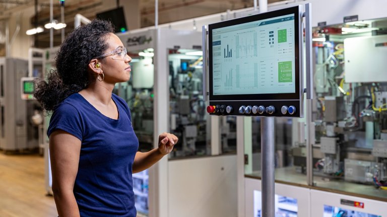 A female operator wearing safety glasses looking at a OptixPanel display in front of an assembly machine.
