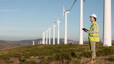 Man with white helmet stand in front of wind farms fields.