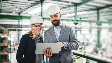A portrait of a mature industrial man and woman engineer with tablet in a factory, working.