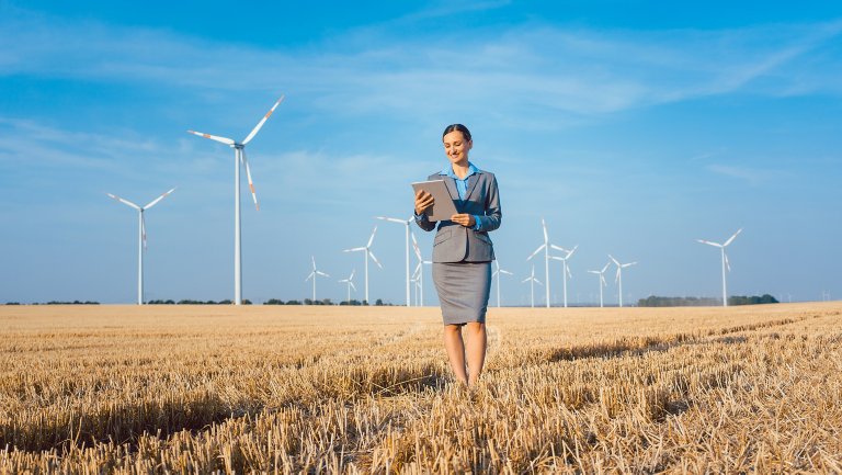 Business woman standing with her computer in a grain field with wind turbines in the background