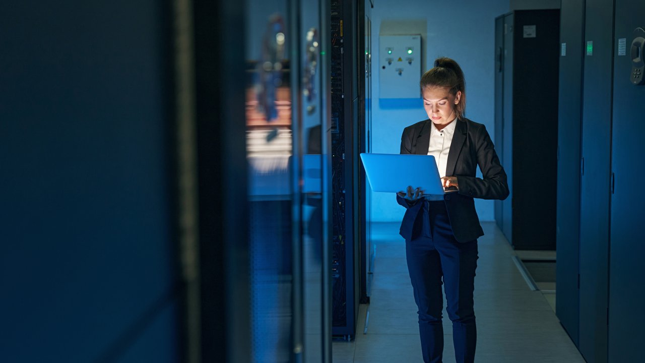 Young woman IT engineer use laptop computer while working with supercomputer in data center server room