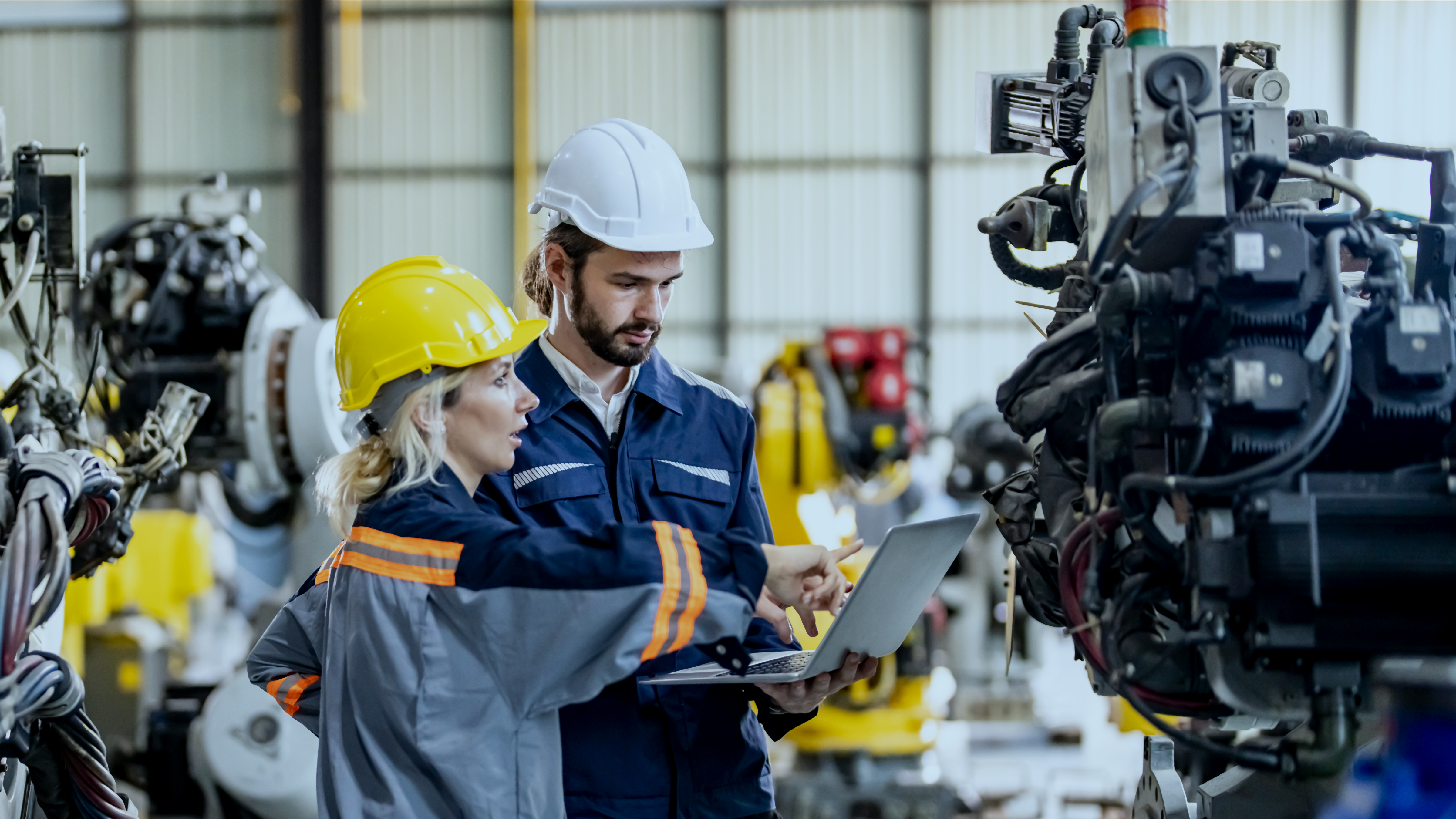 Two workers, a man and a woman, talking to each other inside an industrial machinery room