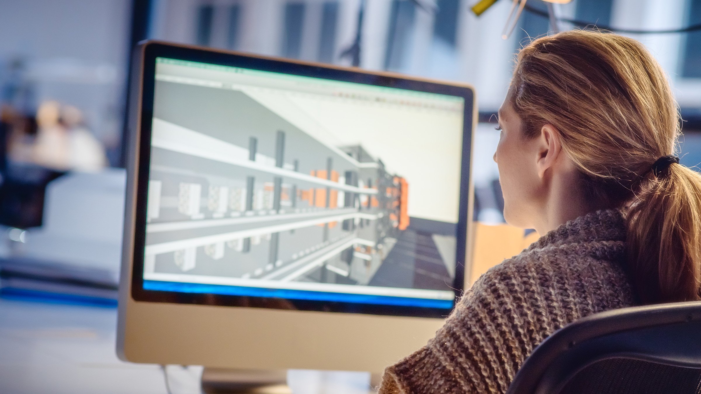 Adult female working on a computer in the office. There is a 3D model on the screen.