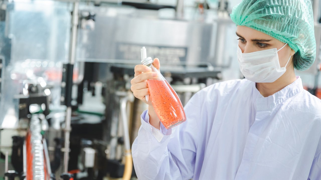 woman-in-ppe-checking-bottle-with-orange-liquid