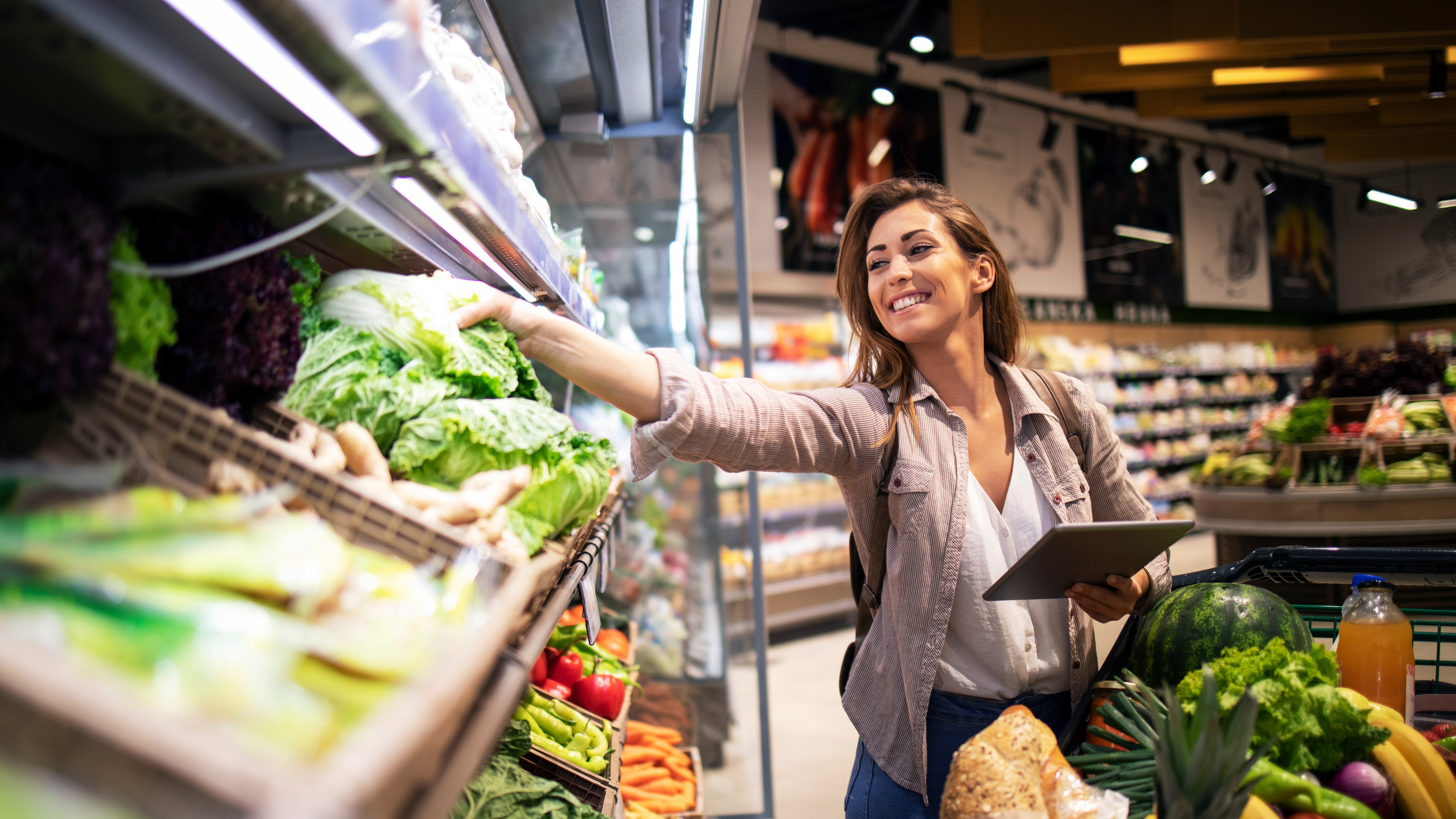 Brunette woman enjoys shopping food at supermarket. Choosing best vegetables on the shelf in grocery store.