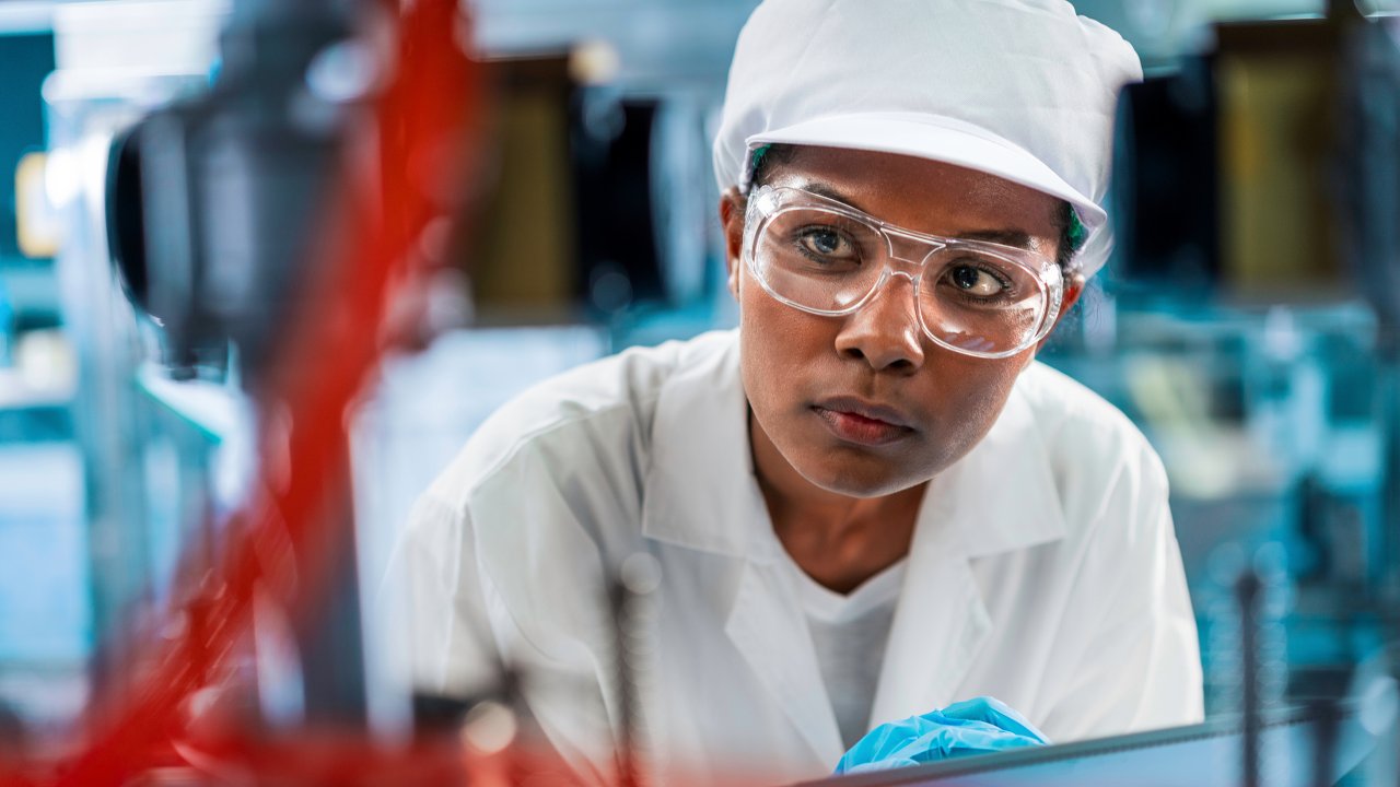 飲用水廠的女工程師穿著專業制服，手拿平板電腦在飲料產業環境中工作。工廠女性員工在生產線中使用平板電腦測試程式。