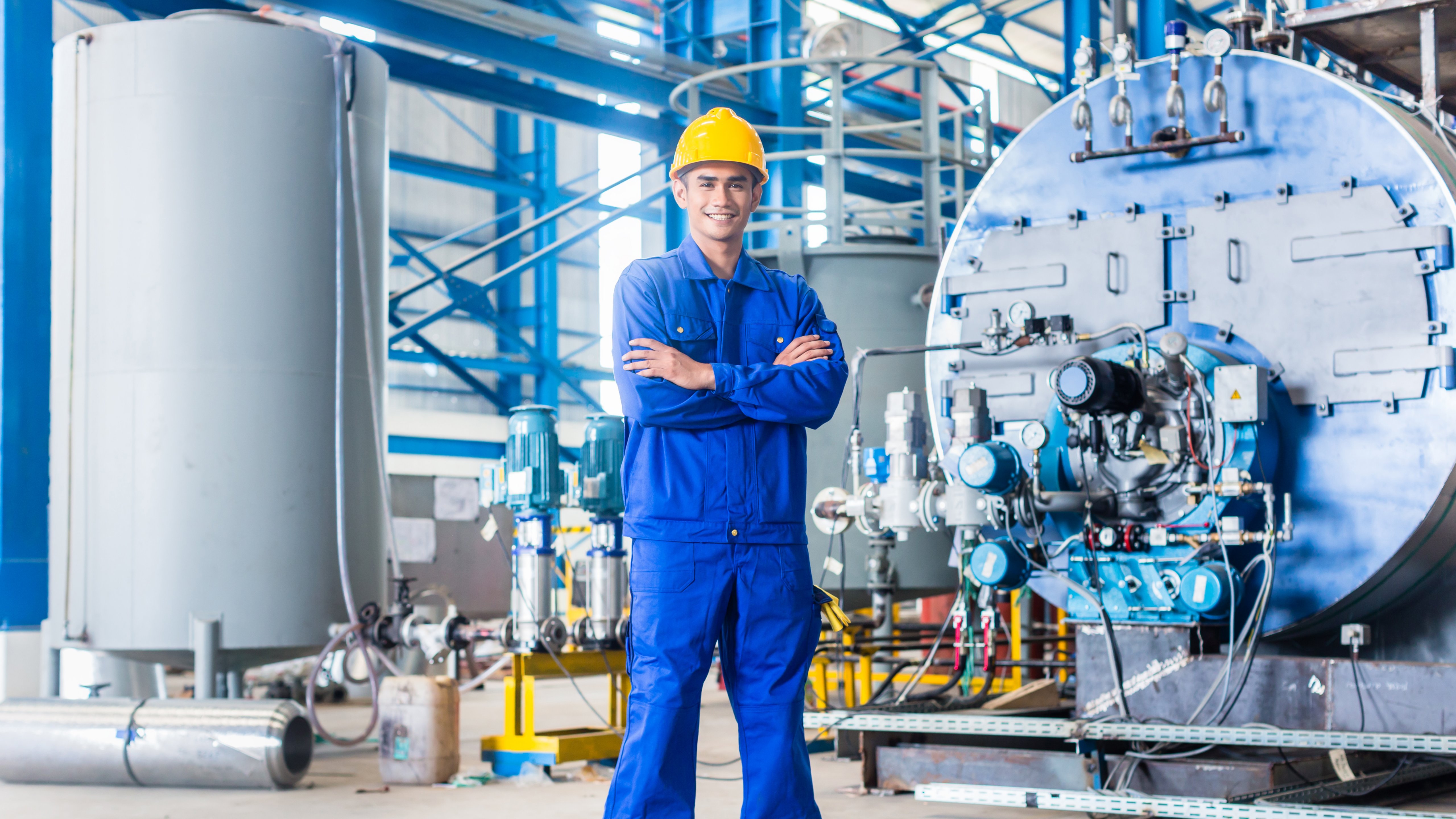 Smiling Asian worker standing in production factory with hard hat and arms crossed