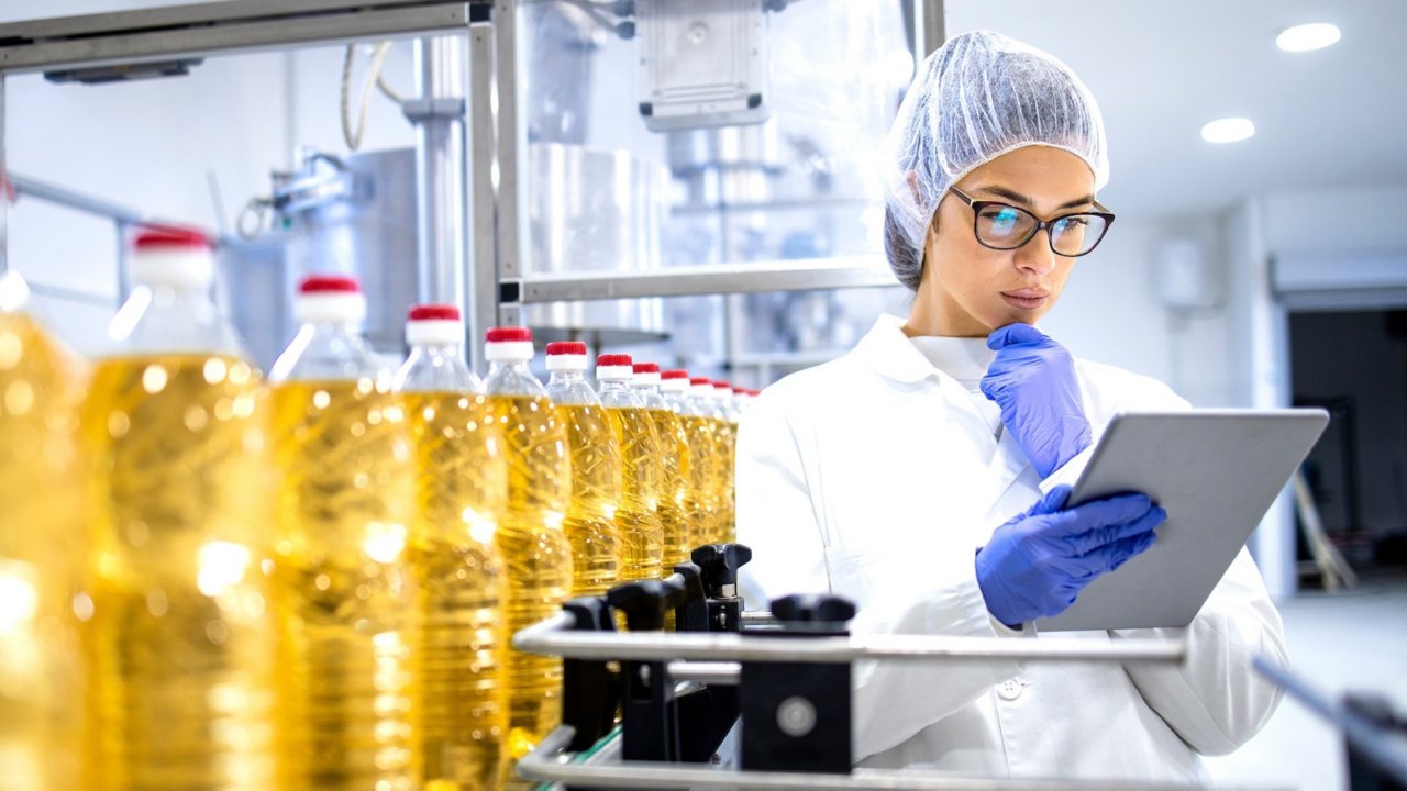 Food factory supervisor or worker holding digital tablet inside refined vegetable oil production plant.