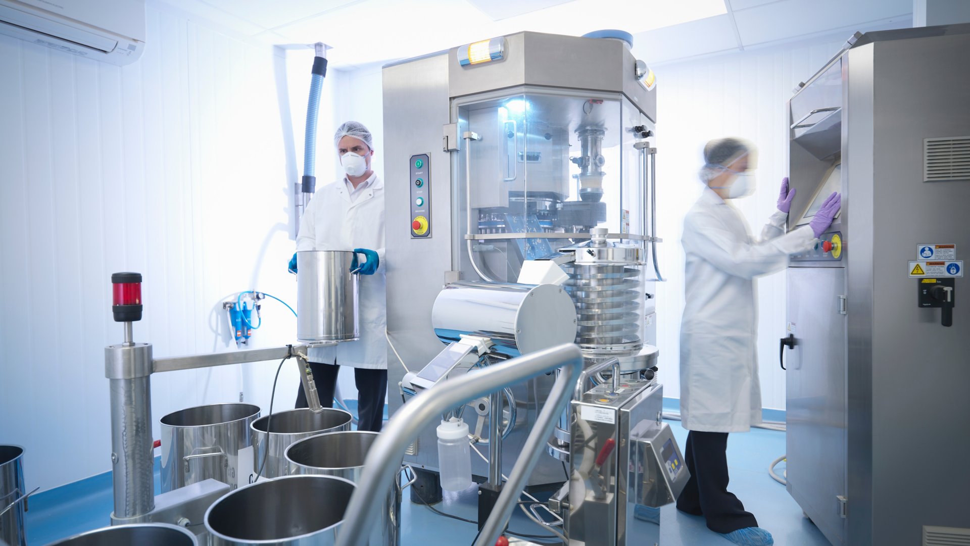 Workers with tablet pressing machine in pharmaceutical factory