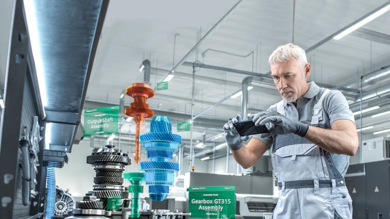 White haired man using smart phone with FactoryTalk Vuforia Factory virtual reality. Image shows the instructions that are seen on screen via VR.