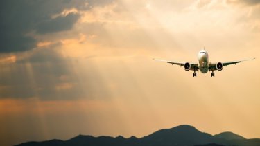 Passenger airplane. Landscape with Front of white airplane is flying in the orange sky with clouds over mountains, sea at colorful sunset. Passenger aircraft is landing. Commercial plane.