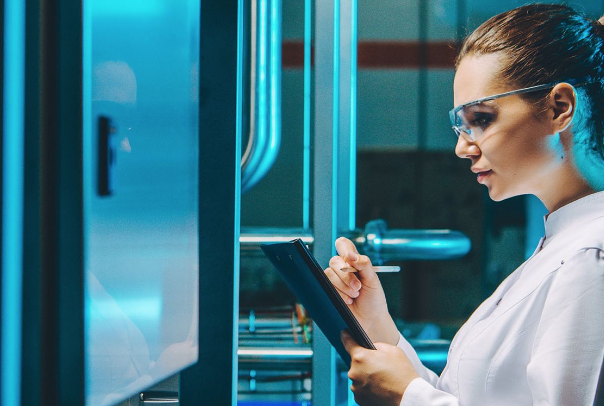 Woman wearing safety glasses and white lab coat holding tablet and stylus
