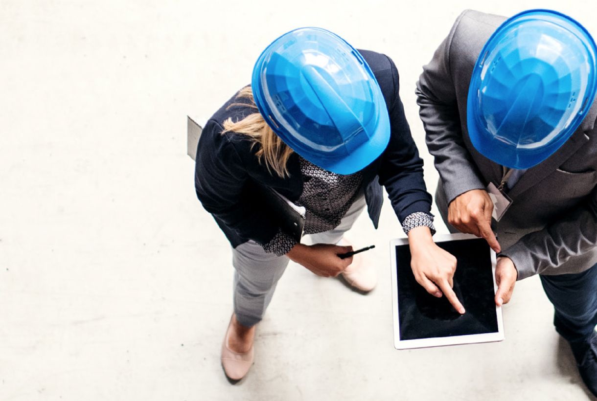 Overhead view of man and woman in blue hardhards looking at tablet