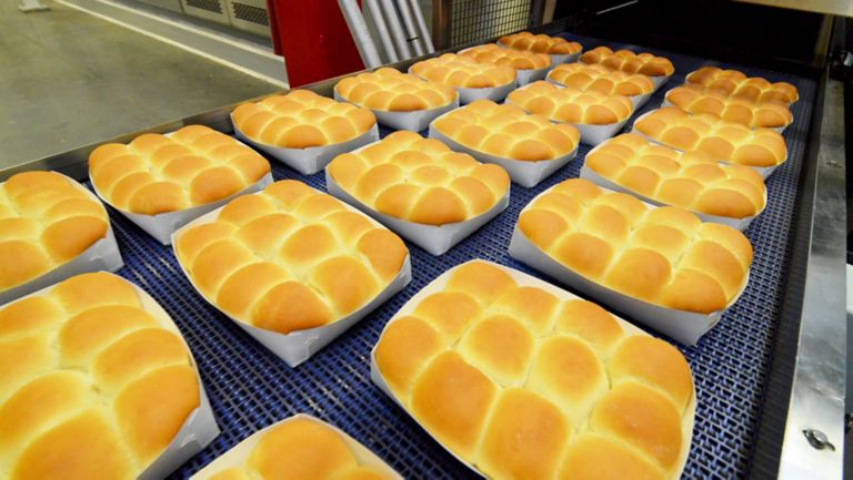 白い段ボール容器に梱包された焼いたパンの並ぶコンベア