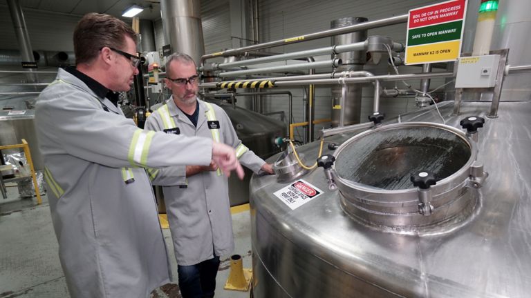 Two male employees viewing a stainless steel vat in a brewery plant