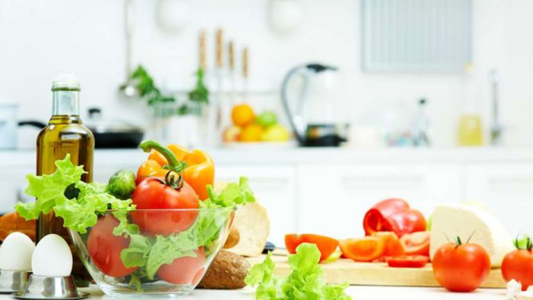 Prepared salad that includes lettuce, tomatoes and eggs in a glass bowl on a white kitchen counter