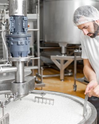 Employee wearing a hair net standing in front of a milk vat