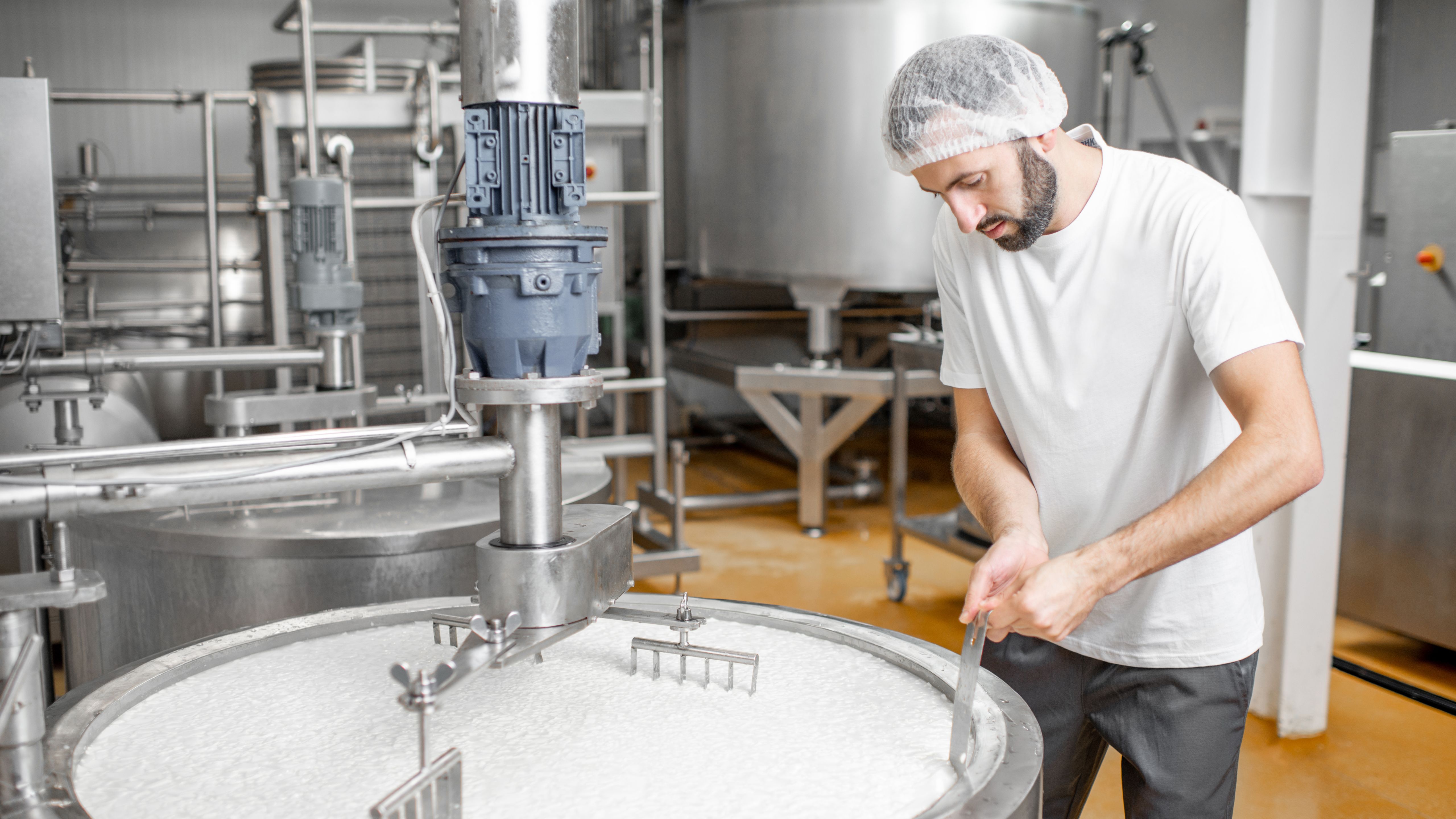 Employee wearing a hair net standing in front of a milk vat