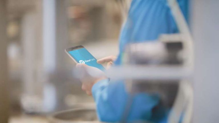 Un empleado con camisa azul viendo un dispositivo móvil con el logotipo de FactoryTalk ViewPoint en la pantalla