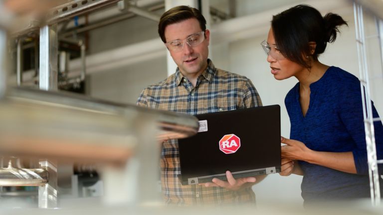 Dos empleados, un hombre y una mujer, observan información en una computadora portátil