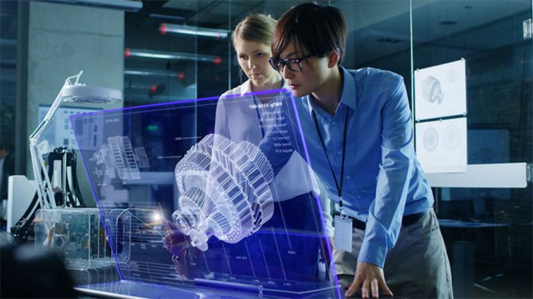 モニタの前で大きな半透明の画像として投影されたコンピュータの情報を見ているオフィスの2人の女性従業員。