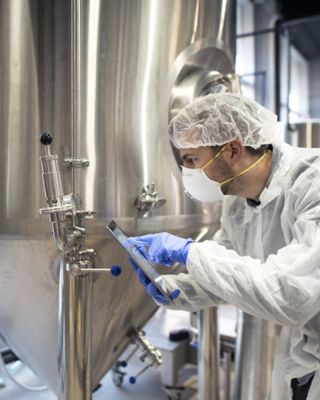 Un empleado con una redecilla, una mascarilla, guantes y una bata blanca en una planta de producción de bebidas