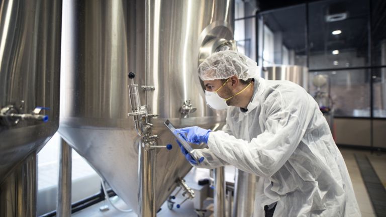 Un empleado con una redecilla, una mascarilla, guantes y una bata blanca en una planta de producción de bebidas