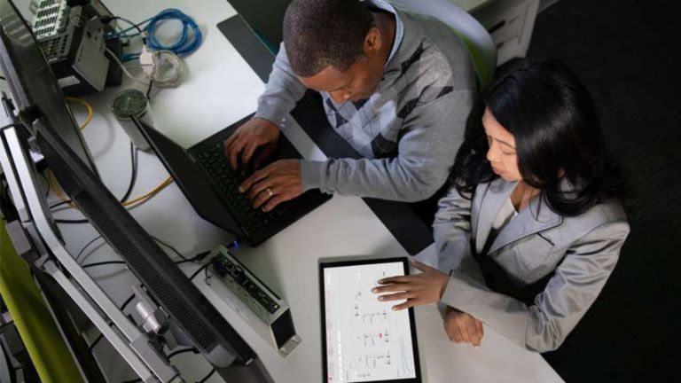 Dois funcionários em uma estação de trabalho analisando dados do software de IHM em um tablet e inserindo os resultados em um laptop