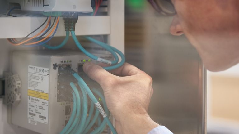 Close-up of worker’s hand and sideview of his face while he connects an Ethernet cable to a Stratix switch for an IT and OT convergence project