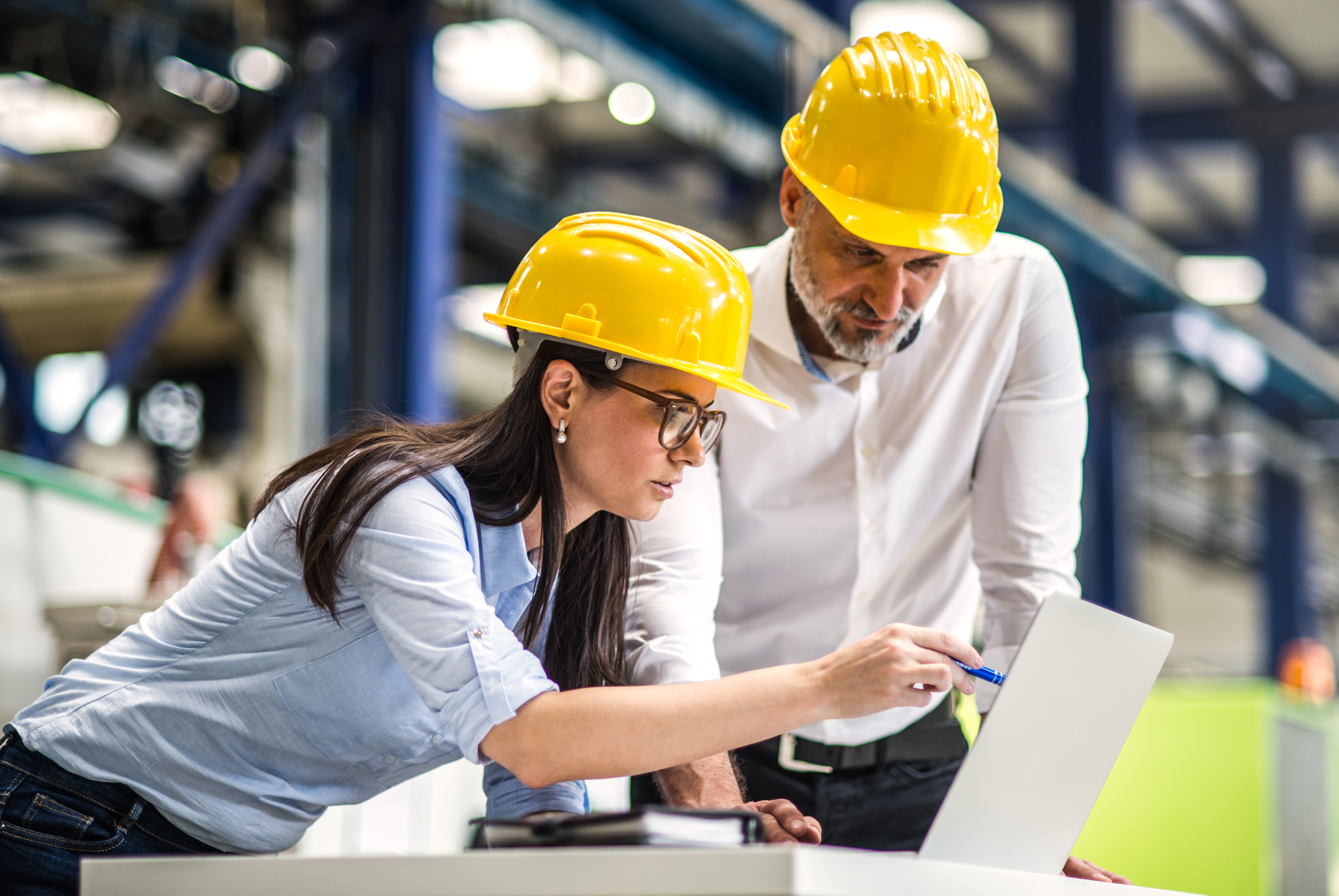 A portrait of an industrial man and woman engineers with laptop in a factory checking documents.