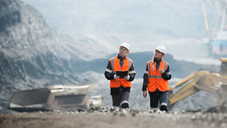 Two mining industry workers walking in an above ground excavation area while holding a handheld tablet and entering information made possible through industrial network solutions