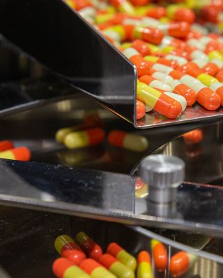 Uma série de pílulas multicoloridas descem por uma esteira metálica como parte da linha de produção de uma fabricante do setor de ciências da vida.