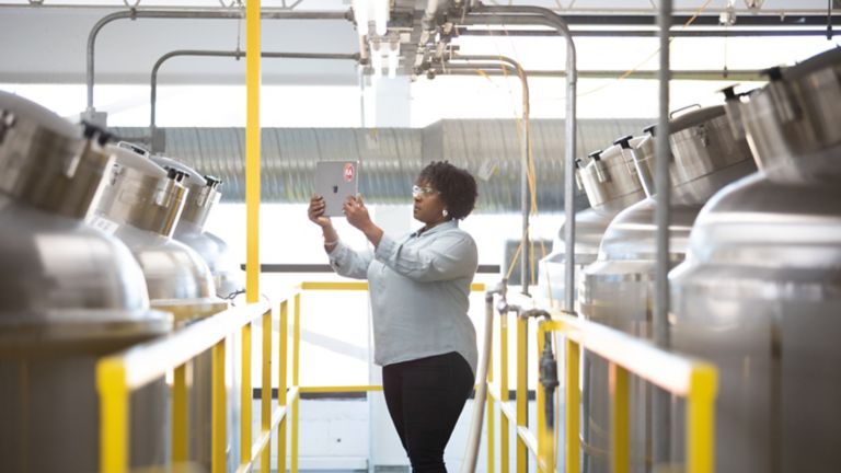 Dipendente donna in piedi in un corridoio in una fabbrica che guarda il suo tablet