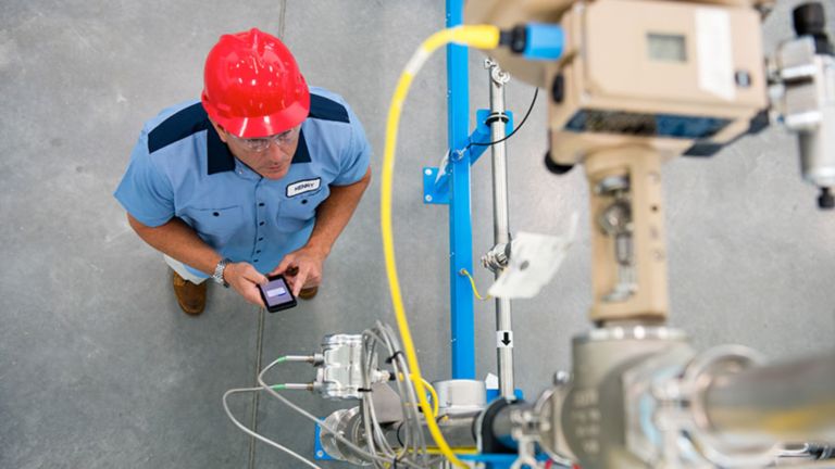 Ein Applikationsingenieur in rotem Schutzhelm und blauer Uniform blickt hoch auf ein Stück Ausrüstung, während er überprüft, dass es sicher funktioniert.
