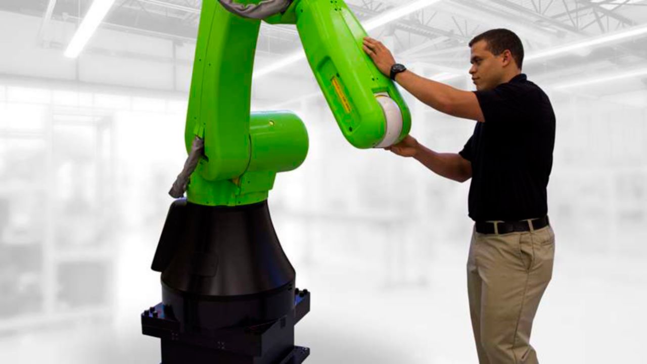 Man inspecting the exterior of a green collaborative robot arm while standing