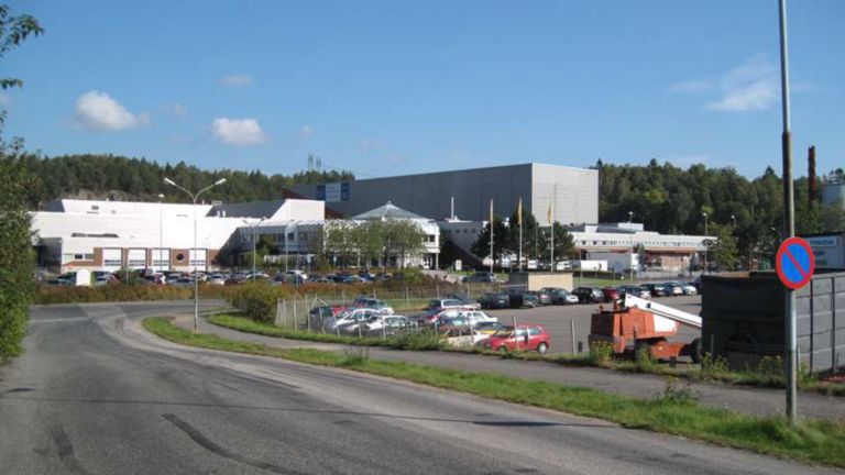 Strada con una curva vicino a un parcheggio pieno di macchine conduce a uno stabilimento Oriola AB nel Regno Unito.